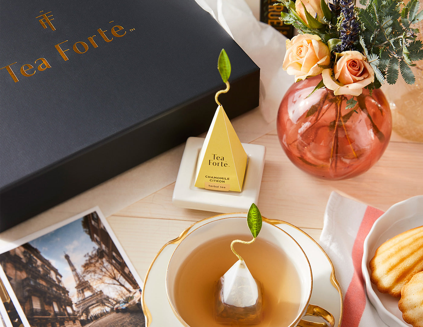 Tea Forté Select Box of 20 pyramid tea infusers, closed on a table with flowers, a fancy teacup and pyramid tea infuser on a Tea Tray