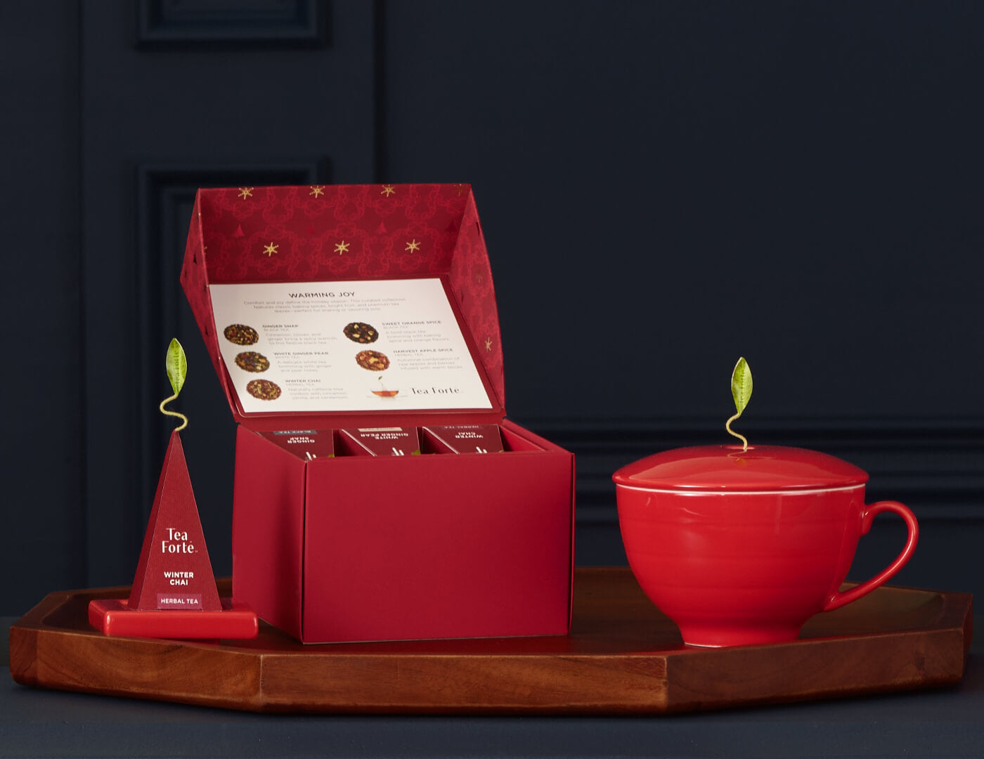 Warming Joy Gift Set with a box of tea and a matching cup on a tray in dark blue background
