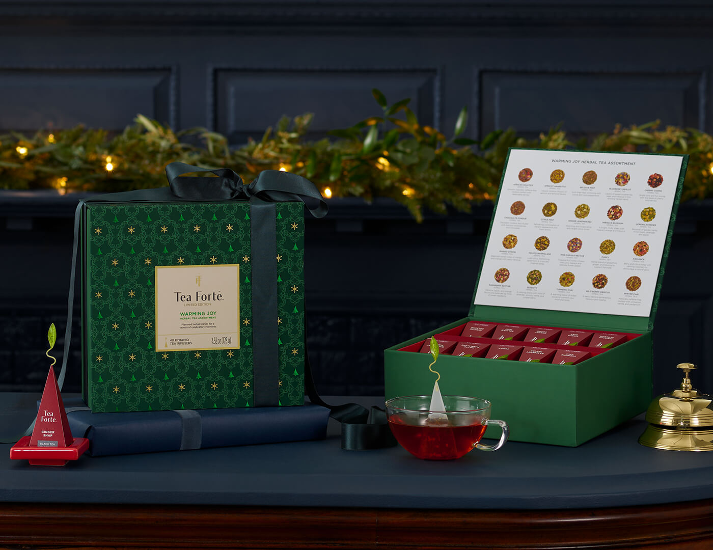Herbal Warming Joy Tea Chests, one wrapped with a ribbon, the other open, with a glass teacup and infuser on a red tray